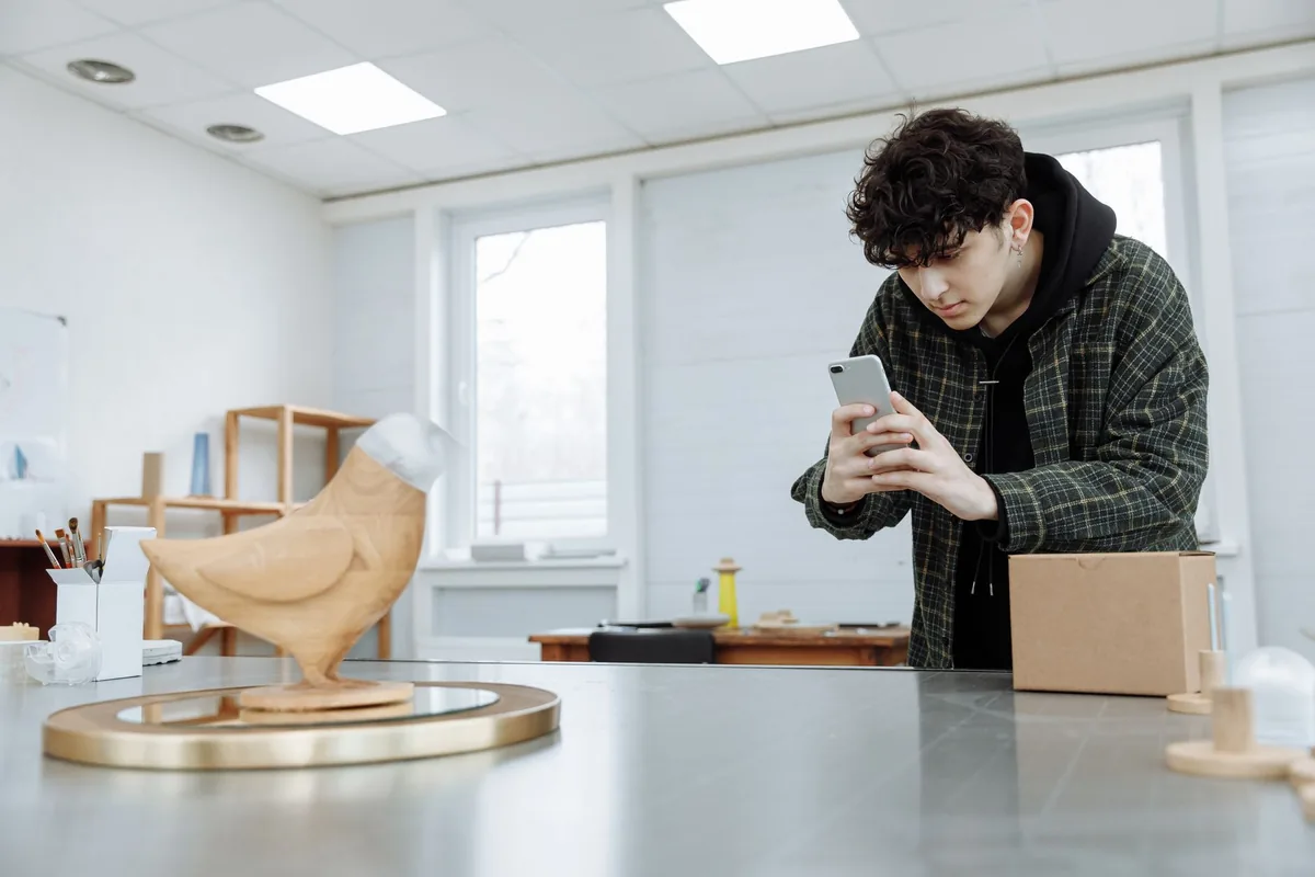 Artisan du bois qui photographie une création avec son téléphone dans son atelier