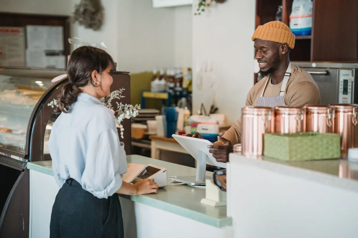 Commerçant qui encaisse une cliente au comptoir de sa petite boutique